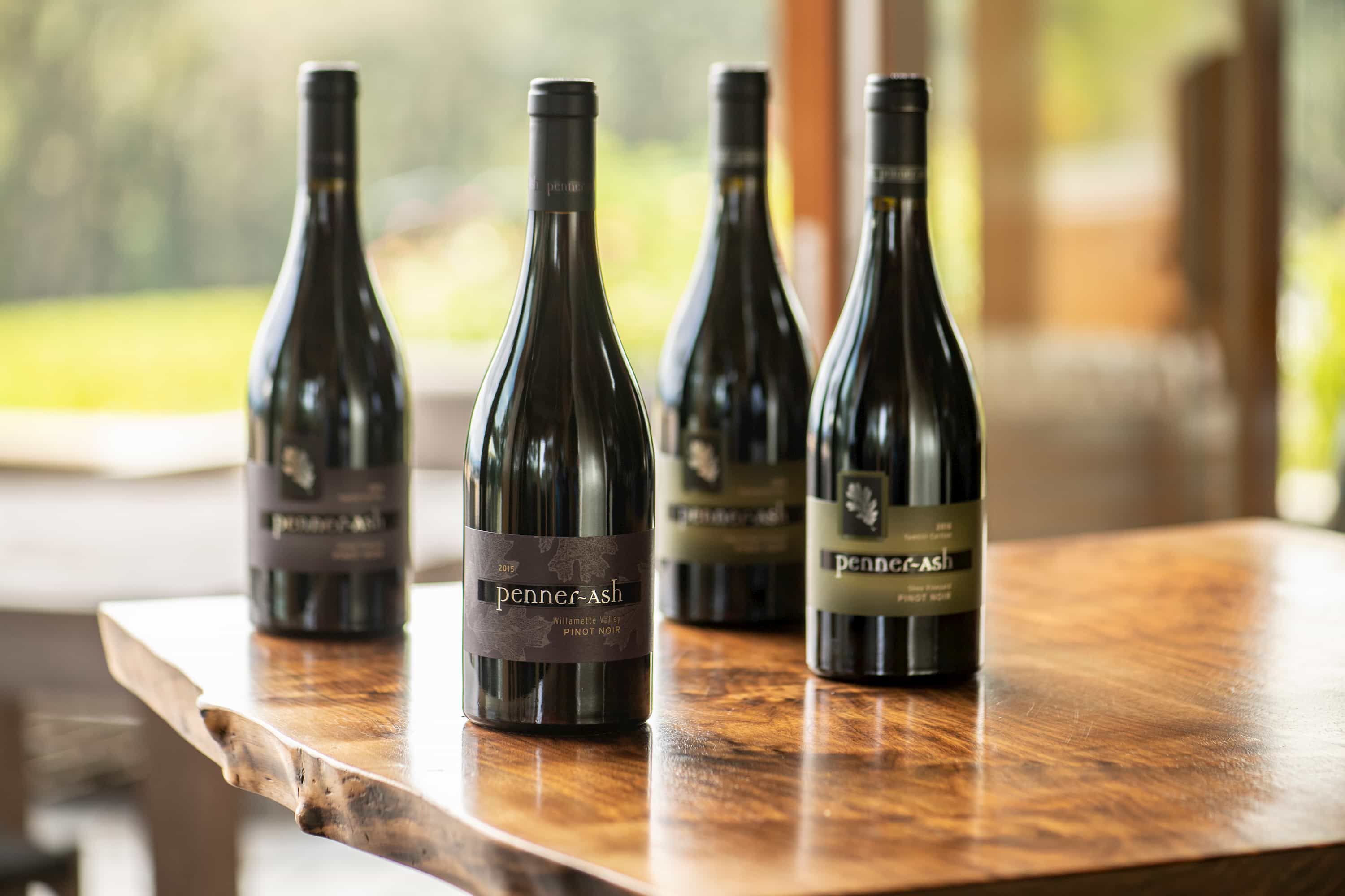 Four bottles of Penner-Ash wine standing on a wooden table.