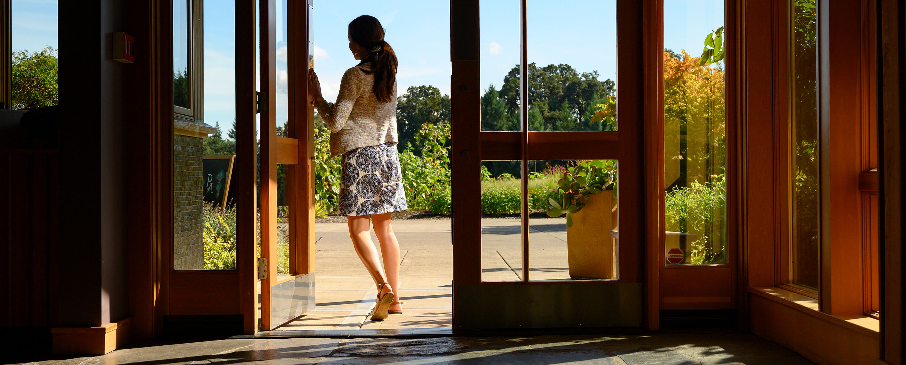 A person opening the Penner-Ash Estate Tasting Room door to go outside.